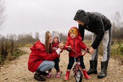 Happy family outdoors with children on a dirt path. Parents supporting kids on a bike ride.