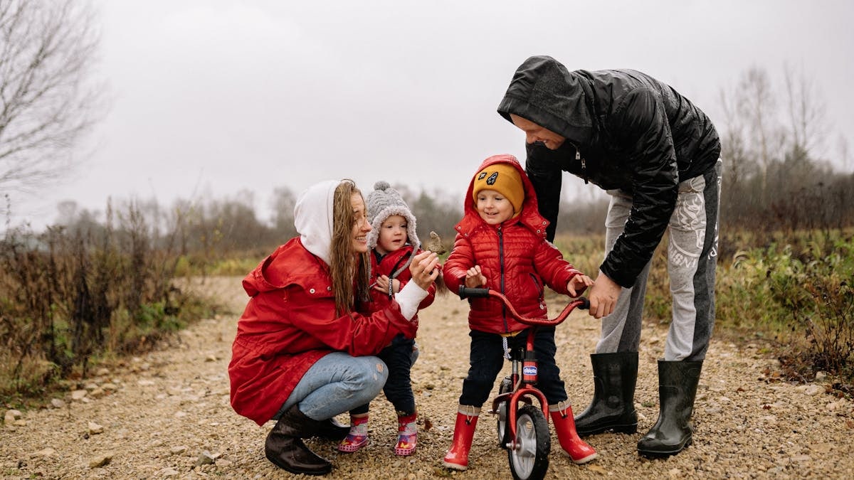 Happy family outdoors with children on a dirt path. Parents supporting kids on a bike ride.